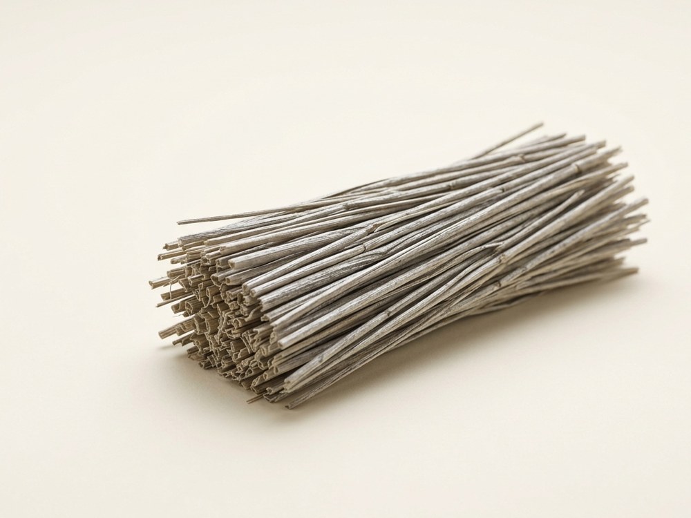 A bundle of dried rice straw, finer and greyer than wheat straw, on a neutral studio background.